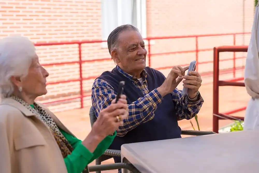 Doi vârstnici la o masă pe terasă, fiecare cu telefonul în mână