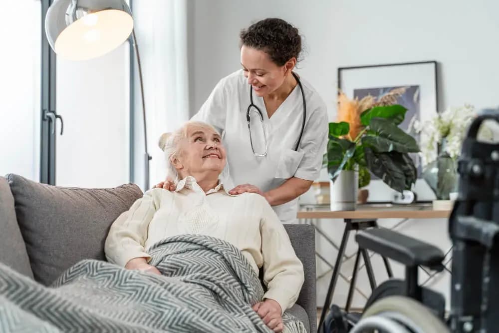 Asistentă medicală lângă o femeie vârstnică așezată pe canapea, acasă